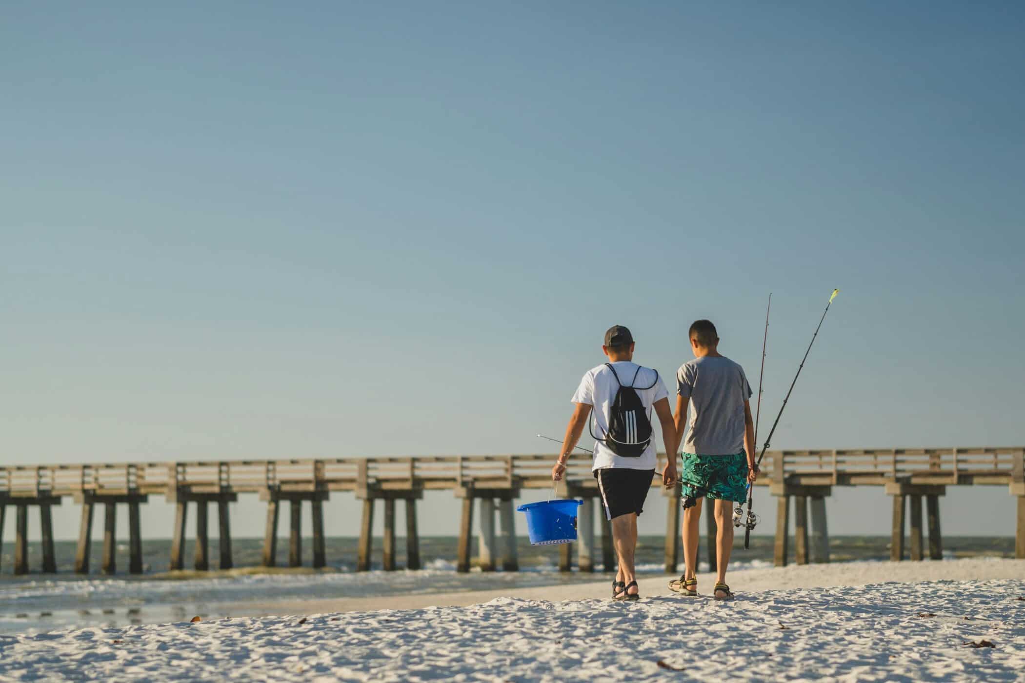 Two anglers carrying fishing rods and a bucket toward a fishing pier on the Outer Banks